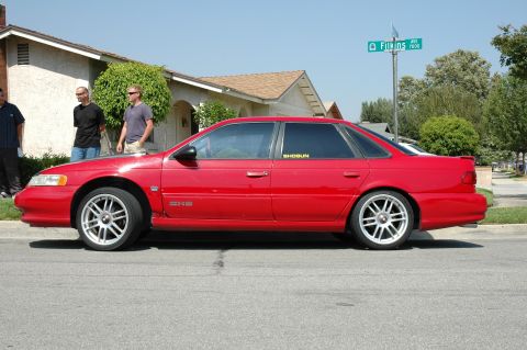 1993 Ford Taurus - A red sedan is parked on a residential street with a street sign visible in the background.