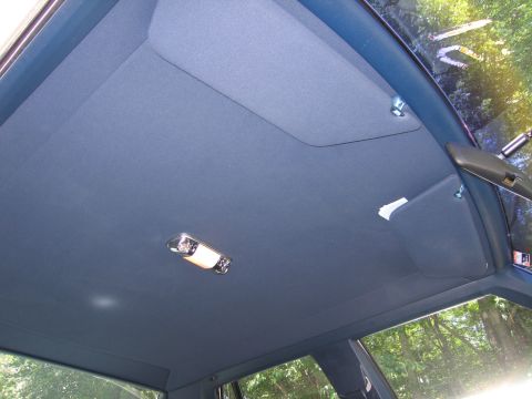 1991 Ford LTD Crown Victoria - The interior ceiling of a vehicle, a dome light and a sun visor, with trees visible through the windows.