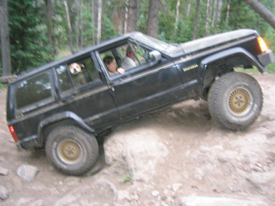 Black Jeep Cherokee navigating a rocky trail with two people and a dog inside