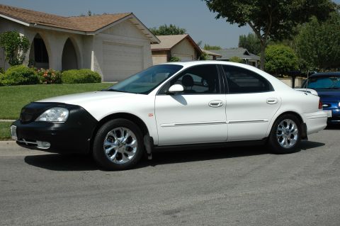 1993 Ford Taurus - A white sedan is parked on a residential street, with a blue car visible behind it.