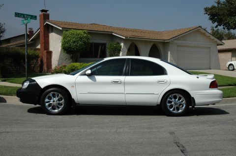 1993 Ford Taurus - A white sedan with a black car bra is parked on the side of a street in front of a house.