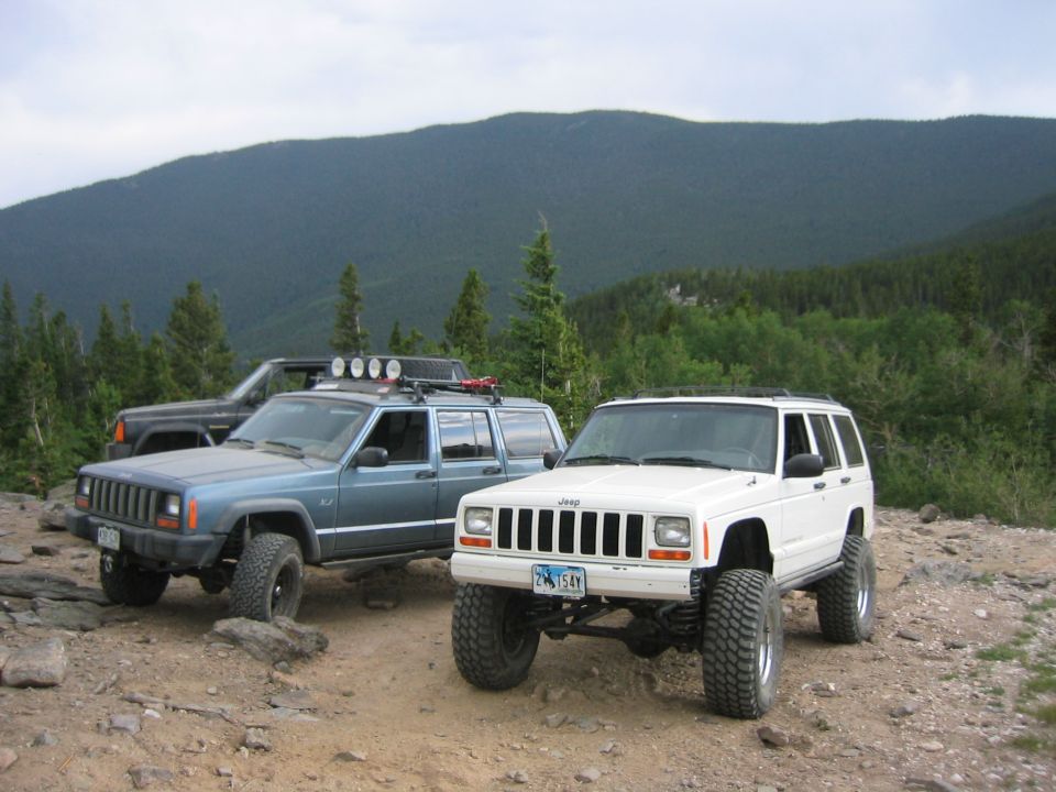 White 1997 Jeep Cherokee with large tires parked on a mountain road