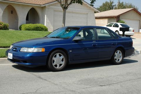 1993 Ford Taurus - A blue sedan is parked in front of a house with a white car in the driveway.