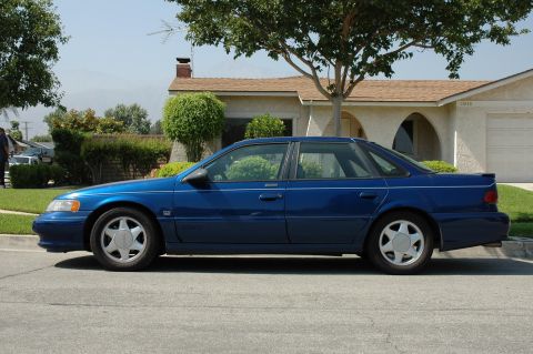 1993 Ford Taurus - A blue sedan is parked on the street in front of a house.