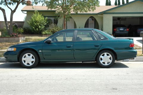 1993 Ford Taurus - A green 1993 Ford Taurus is parked on the street in front of a house.