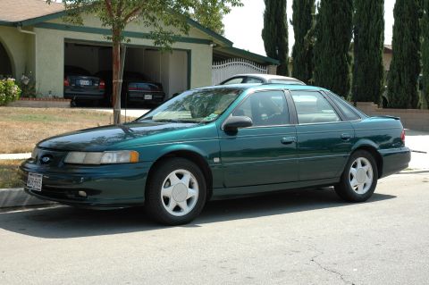 1993 Ford Taurus - A green sedan is parked on the street in front of a house with a garage.