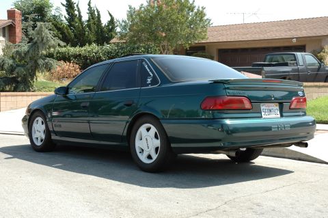 1993 Ford Taurus - The rear of a green sedan is visible, parked on a residential street with a truck in the background.