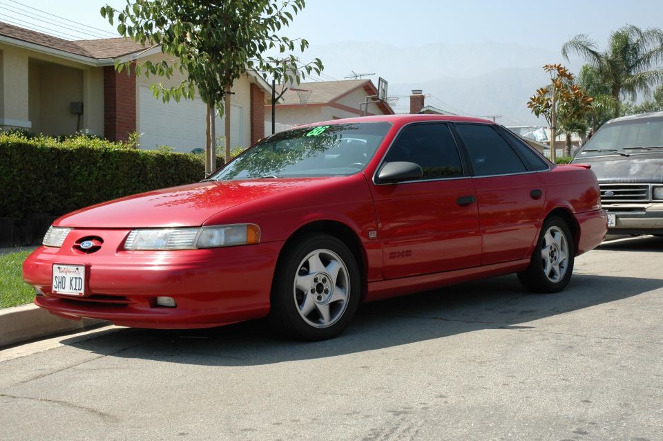 Red sedan parked on a street, front 3/4 view. The car has tinted windows and a license plate reading "SHO KID"