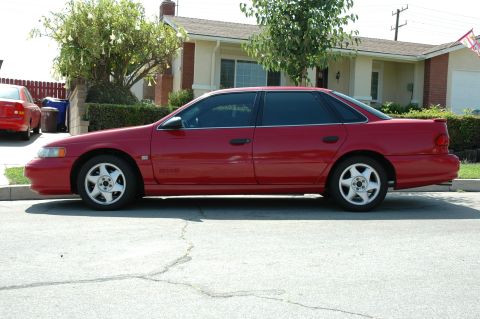 1993 Ford Taurus - Side profile of a red sedan, likely a 1996 Ford Taurus, parked on a residential street.