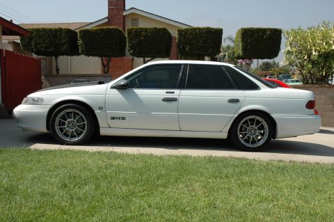 1993 Ford Taurus - Side view of a white sedan with aftermarket wheels and a black hood accent.