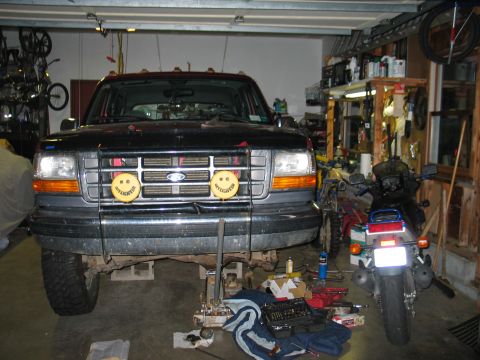 1995 Ford Bronco - Front view of a black full-size Ford Bronco raised on jack stands inside a home garage, its front end fitted with a tubular brush guard hol…