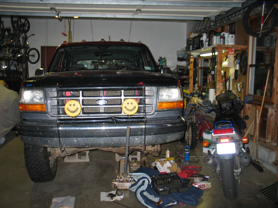 Black Ford Bronco on jack stands in garage, brush guard with KC driving lights, front view