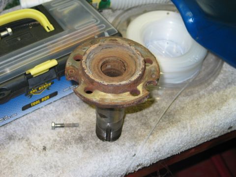 1995 Ford Bronco - A corroded steel wheel hub and spindle assembly with rusty bearing surfaces sits on a shop bench beside a plastic tool box and a hex bolt,…