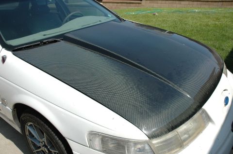 1993 Ford Taurus - A white sedan is parked outside with a carbon fiber hood and a blue emblem on the front.