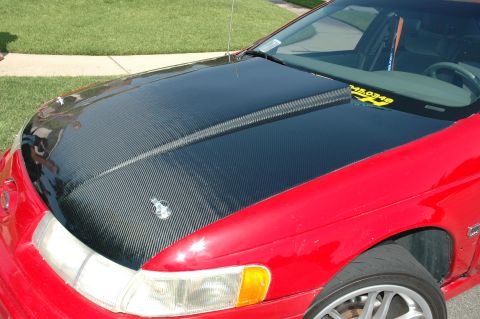 1993 Ford Taurus - A red 1993 Ford Taurus is shown from the front with a carbon fiber hood and a yellow sticker on the windshield.