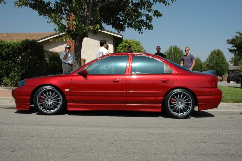 1993 Ford Taurus - A red sedan is parked on the street, its custom wheels and spoiler.