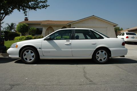 1993 Ford Taurus - A white 1993 Ford Taurus is parked on a residential street with a house and another car in the background.