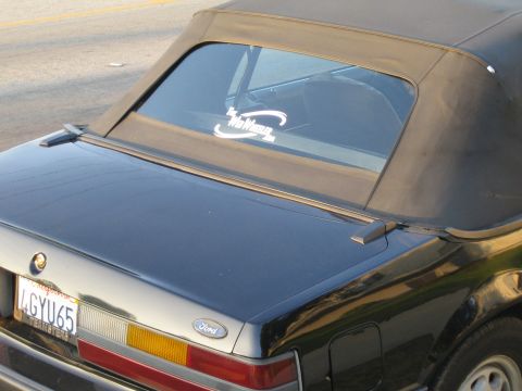 1985 Ford Mustang - A black convertible car's rear is shown with a sticker on the back window.