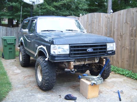 1988 Ford Bronco - A lifted Ford Bronco is parked in a driveway, appearing to be undergoing some maintenance or modification.