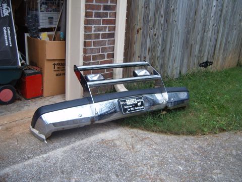 1988 Ford Bronco - A detached Ford Bronco bumper with a brush guard is placed on the ground next to a brick wall and wooden fence.
