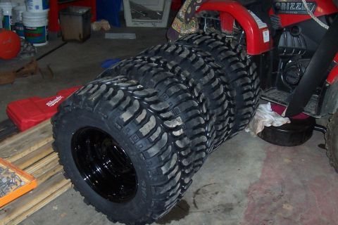1994 Ford F-150 - A stack of four aggressive tread tires are leaning against a red ATV in a garage.