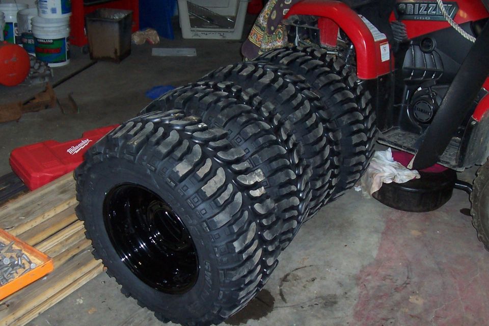 stack of four off-road tires with black rims, leaning against a red ATV