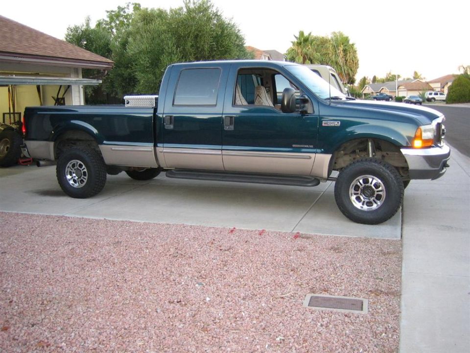 Dark green Ford Super Duty crew cab long-bed pickup parked in profile on a driveway.