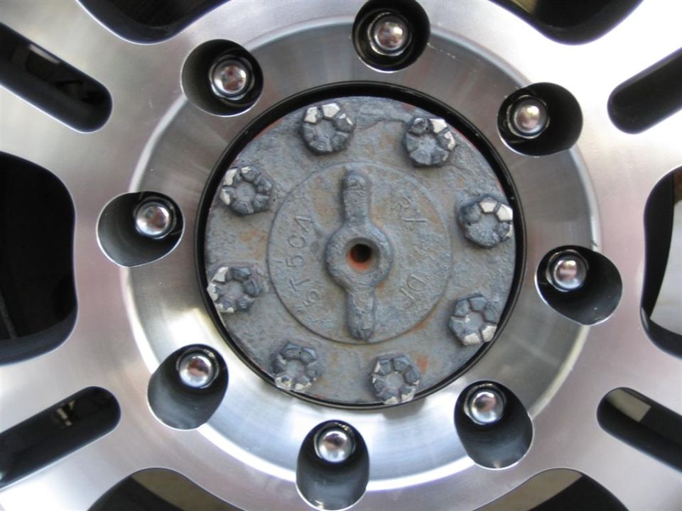 Center of an 8-lug aluminum wheel showing chrome lug nuts and a weathered bolt-on front hub