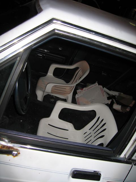 1991 Ford LTD Crown Victoria - The interior of a vehicle is shown, with two white plastic chairs placed inside and a steering wheel visible.