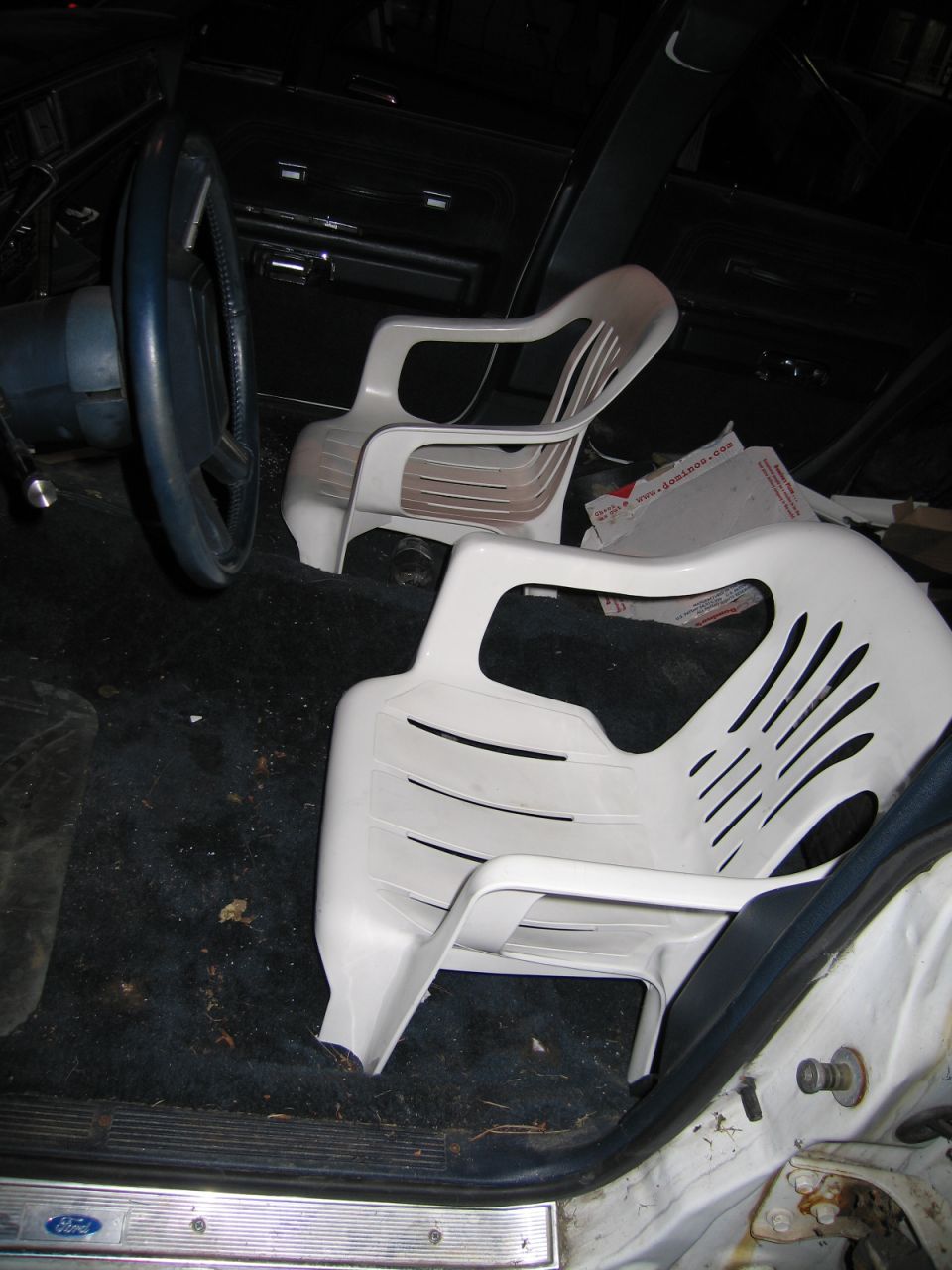 Interior of a car with two white plastic chairs placed in the front seats. Ford logo visible on the door sill