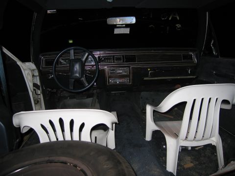 1991 Ford LTD Crown Victoria - The interior of a car is shown with two white plastic chairs placed in the front seats, and a spare tire visible.