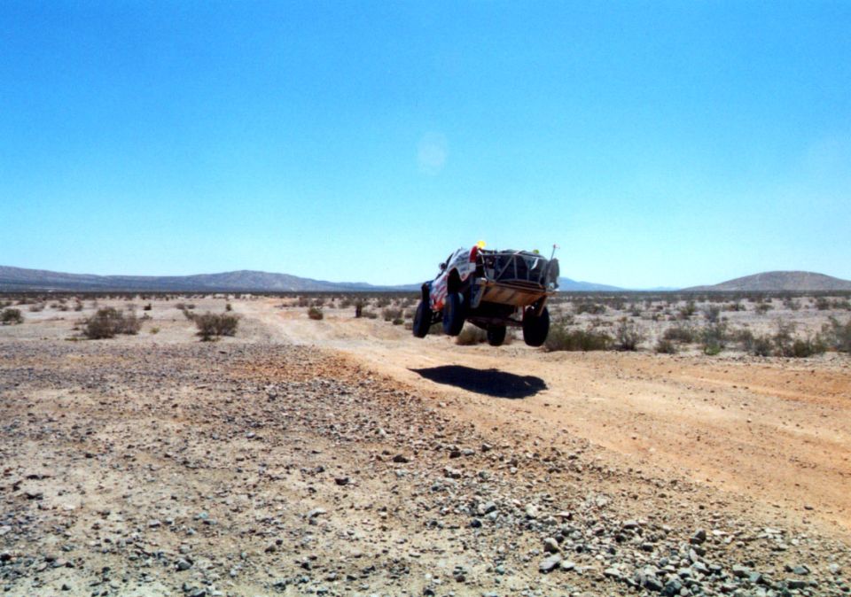 Off-road race truck airborne over a dirt berm in an open desert landscape