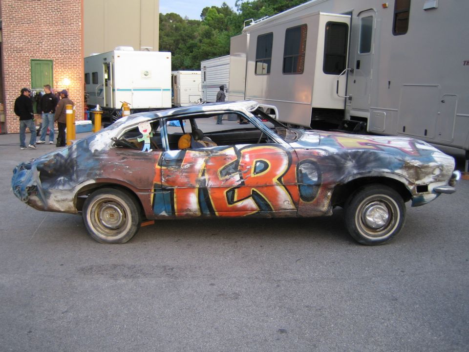 Side view of a battered graffiti-painted Ford Maverick fastback in a back lot