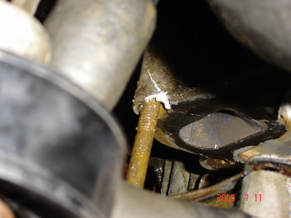 Rusty bolt protruding from a corroded engine component with white sealant