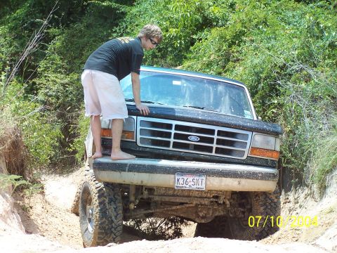 1987 Ford Bronco - A person stands on the hood of a lifted Ford truck, which appears to be from the early to mid-1990s.