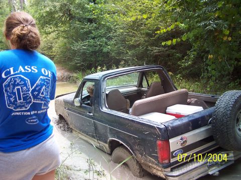 1987 Ford Bronco - A dark blue Ford Bronco is stuck in mud with a person in the driver's seat and two coolers in the bed.