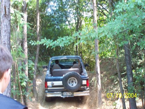 1987 Ford Bronco - This 1987 Ford Bronco is captured from the rear as it navigates an off-road trail, kicking up dirt.