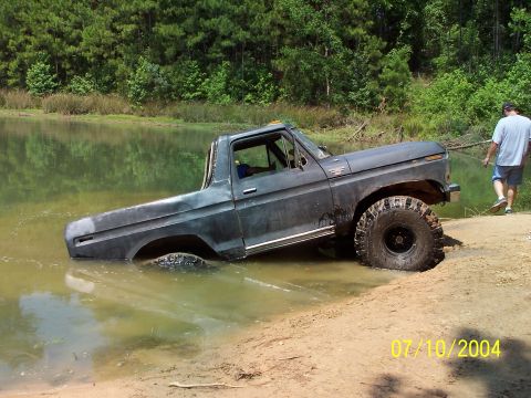 1987 Ford Bronco - Ford Bronco partially submerged in water, with a person standing on the bank.