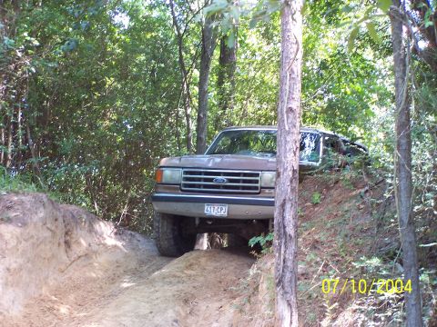 1987 Ford Bronco - A brown 1987 Ford Bronco navigates a challenging off-road trail through the woods.