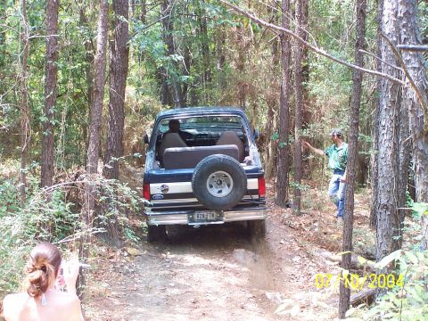 1987 Ford Bronco - A 1987 Ford Bronco navigates a wooded trail, kicking up dust from the rear.