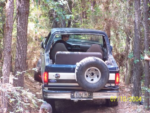 1987 Ford Bronco - This 1987 Ford Bronco is seen from the rear, navigating a wooded trail with its spare tire mounted on the back.