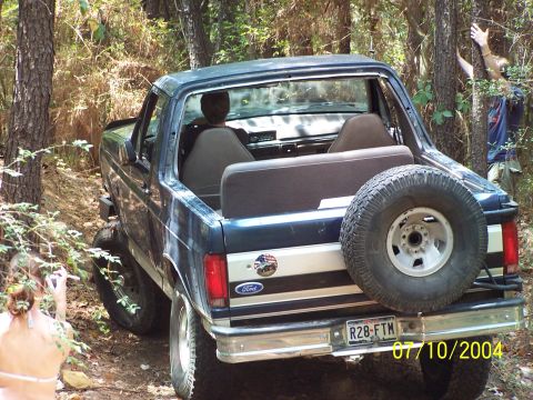 1987 Ford Bronco - 1987 Ford Bronco navigating a wooded trail with a spare tire mounted on the rear.