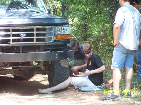 1987 Ford Bronco - Two men work on the front bumper of a 1992 Ford F-150 in a wooded area.