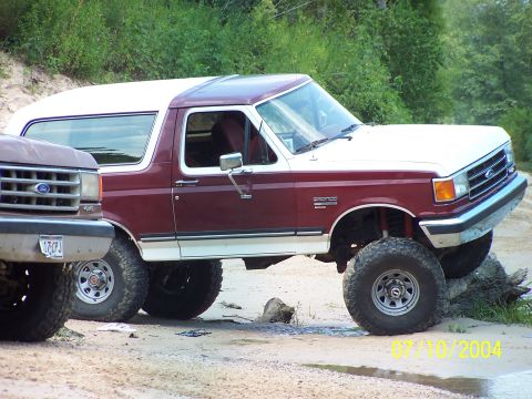 1987 Ford Bronco - This lifted 1987 Ford Bronco is navigating rough terrain, with another Ford truck nearby.