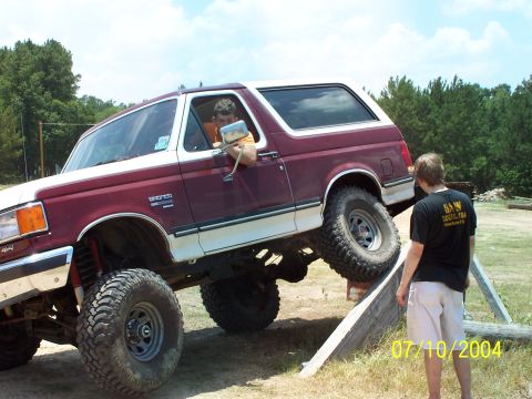 1987 Ford Bronco - A maroon and white 1987 Ford Bronco is shown with a lifted suspension, navigating an off-road course.