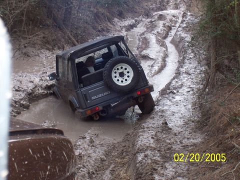 1987 Ford Bronco - A Suzuki Samurai is stuck in a muddy off-road track, with another vehicle partially visible in the foreground.