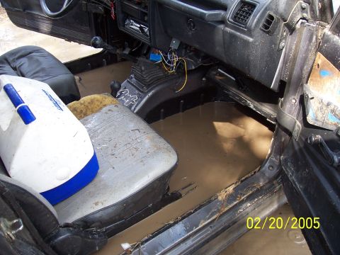 1987 Ford Bronco - The interior of a vehicle is filled with mud and water, suggesting it has been submerged or driven through deep mud.