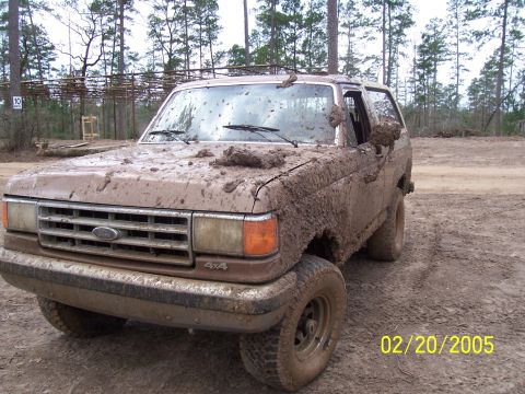 1987 Ford Bronco - A heavily muddied 1987 Ford Bronco sits in a dirt lot, its body covered in mud.