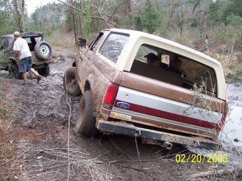 1987 Ford Bronco - Two off-road vehicles are stuck in the mud on a trail.