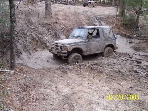 1987 Ford Bronco - A Suzuki Samurai navigates a difficult muddy terrain, with other off-road vehicles visible in the distance.